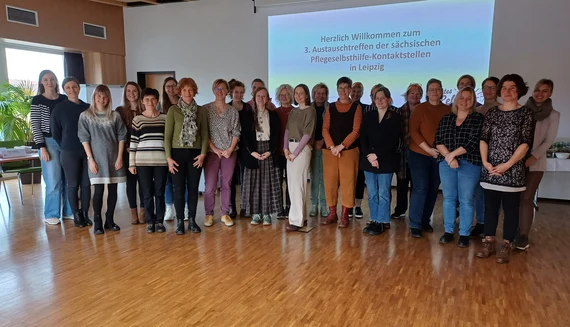 Teilnehmende des 3. Austauschtreffens sächsischer Pflegeselbsthilfe-Kontaktstellen in Leipzig stehen nebeneinander vor Leinwand.