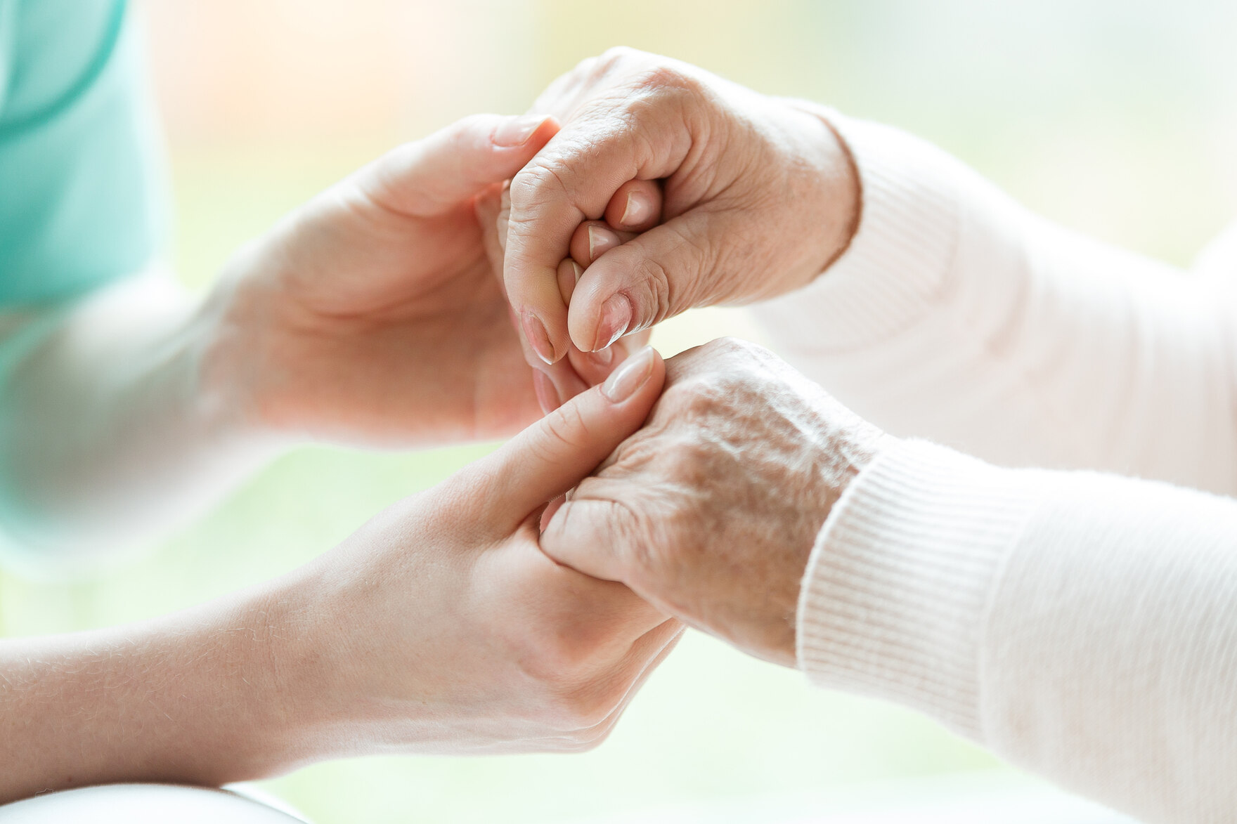 Eine Pflegekräft hält die Hände einer älteren Person und es sind nur ihre Hände zu sehen
