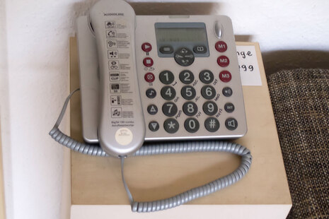 Zu sehen ist ein Telefon, auf dem die Tasten besonders groß sind. Auf dem Hörer sind Hinweise zur Nutzung aufgeklebt.