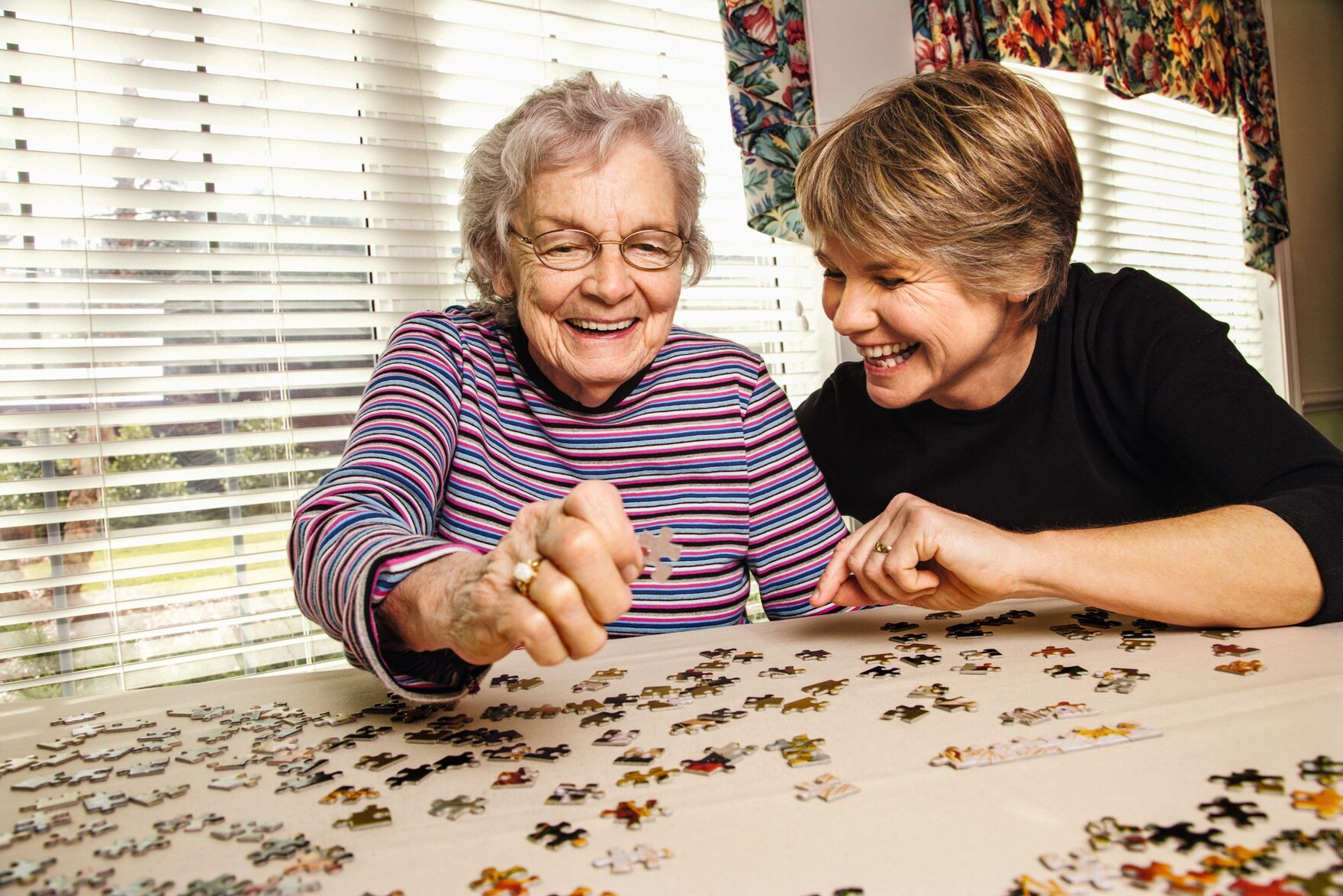 Seniorin und Alltagsbegleiterin puzzeln gemeinsam