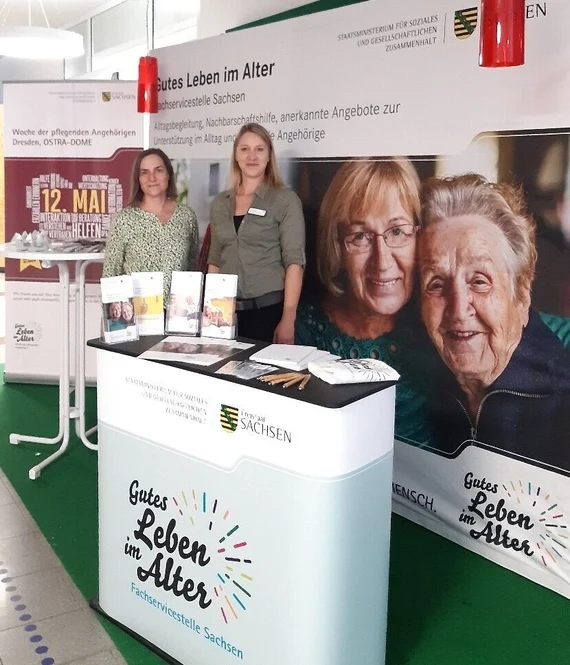 Zwei Mitarbeiterinnen am Informationsstand der Fachservicestelle Sachsen „Gutes Leben im Alter" mit Infomaterial und Plakatwand beim SZ-Aktionstag..