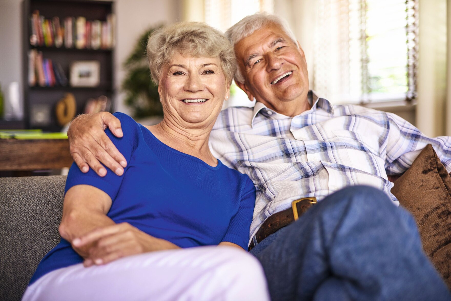 Eine ältere Frau und ein älterer Mann sitzen nebeneinander und lachen. Der Mann hat einen Arm um die Frau gelegt.
