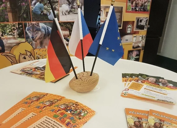 Tisch mit deutschen, tschechischen und EU-Flaggen sowie Informationsmaterialien bei deutsch-tschechischem Austauschtreffen.