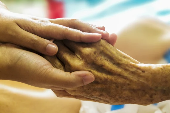 Junge Hände halten schützend ältere Hand einer Seniorin in warmem Licht.