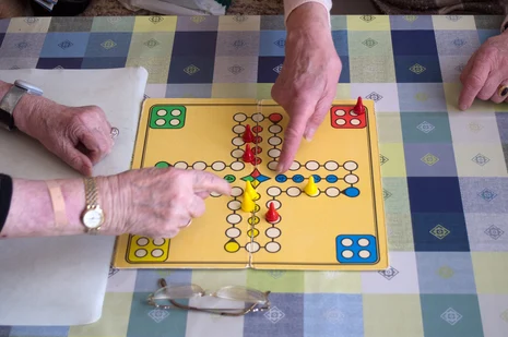 Vier Personen spielen gemeinsam "Mensch ärgere Dich nicht" auf karierter Tischdecke.